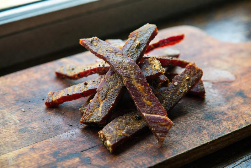 Premium kosher beef jerky strips on a rustic wooden board high-quality snack photography.